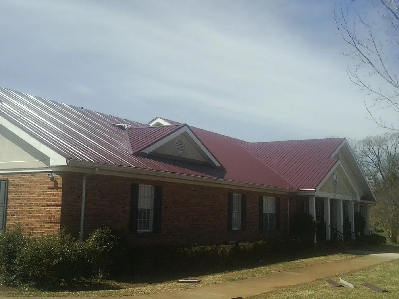 Red metal roof with gabled entries on a long brick building, from a Hail Damage Roof Repair job in Port Arthur