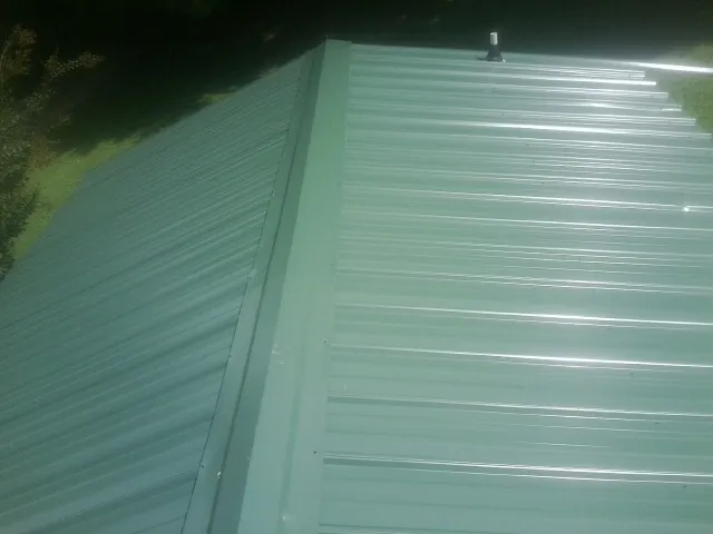New green metal panels meeting at the ridge of a roof — Flat Roof Repair work by our crew in Port Arthur