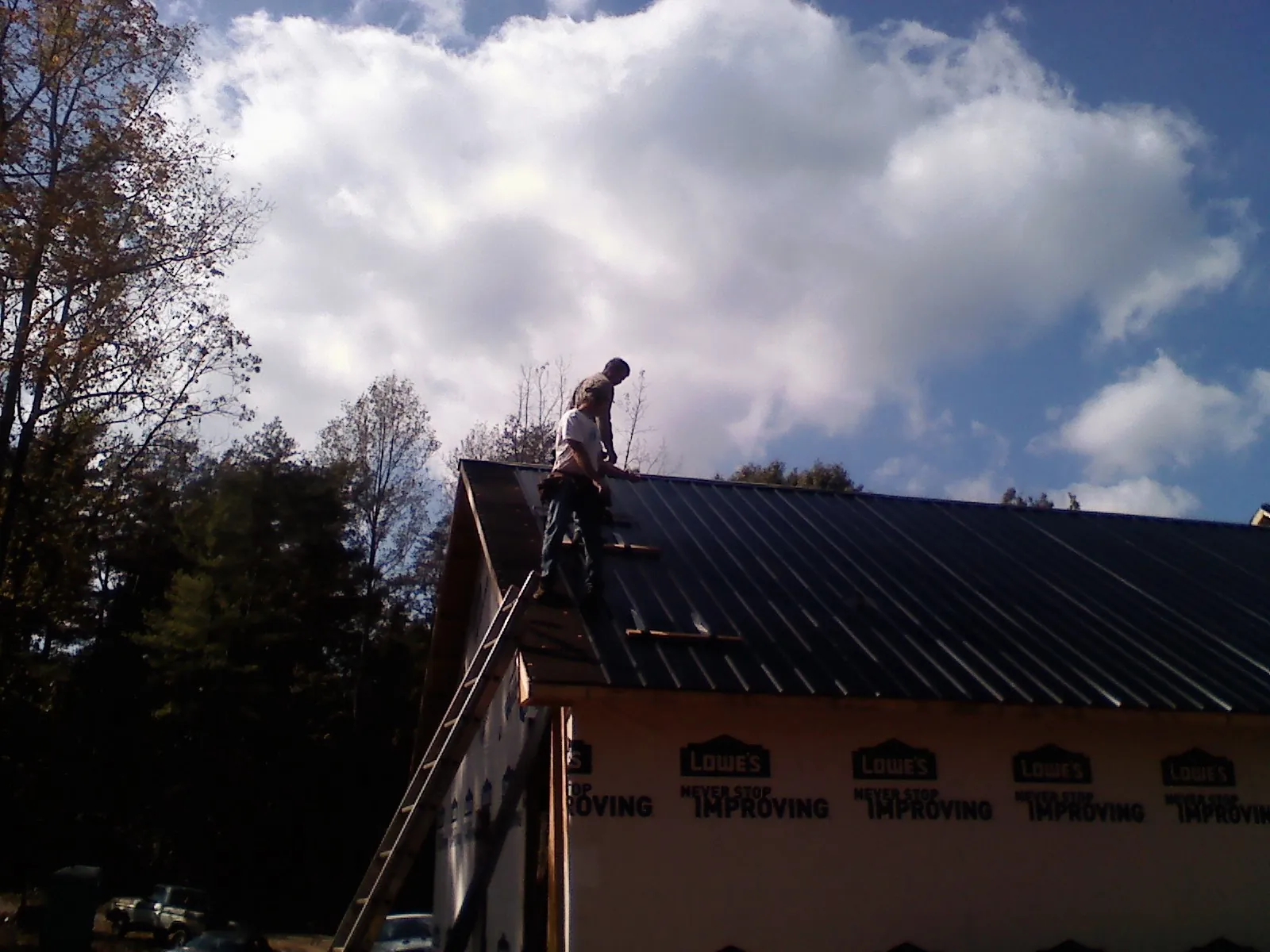 Roofer fastening dark metal panels high against a cloudy sky, from a Roof Inspection job in Port Arthur