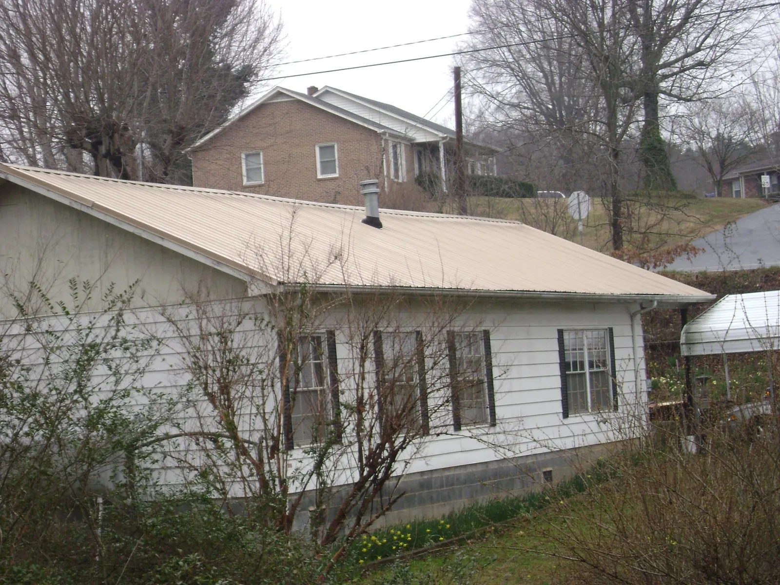 Tan metal roof on a white sided house set into a hillside — Commercial Roofing by Roofing Brothers in Port Arthur