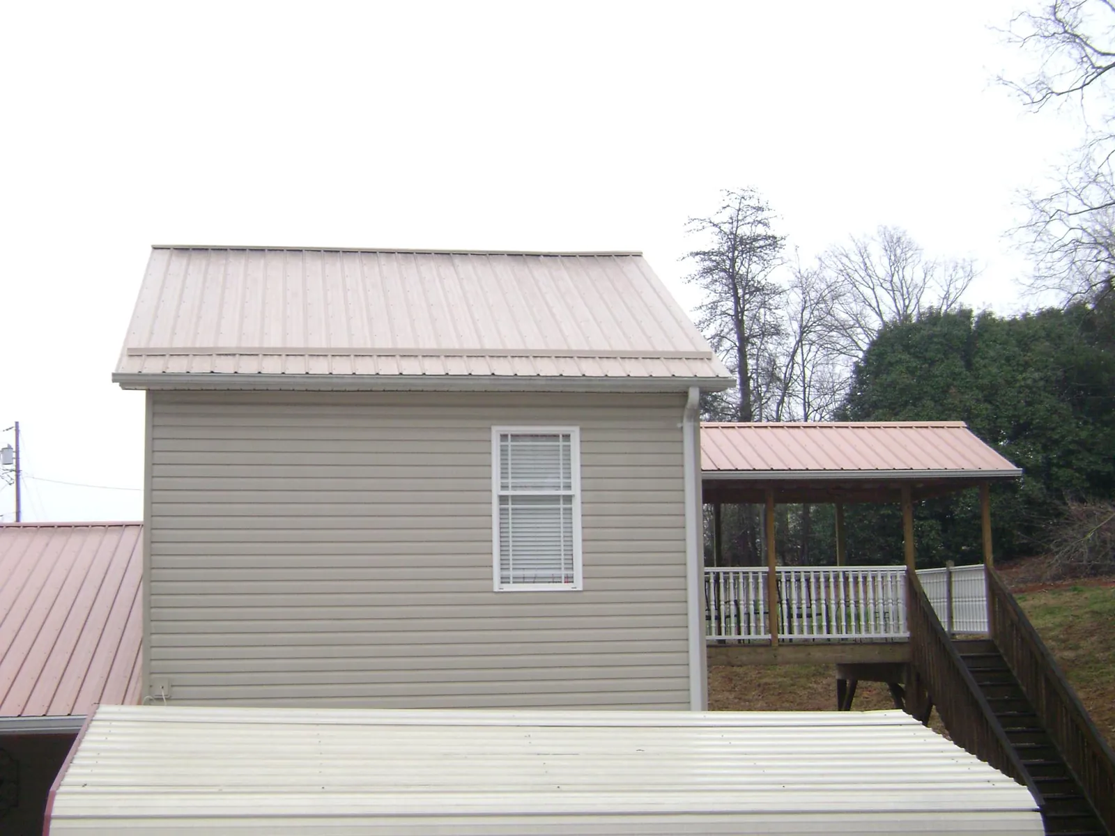Tan metal roofs on a two story addition and attached porch, from a Roof Replacement job in Port Arthur